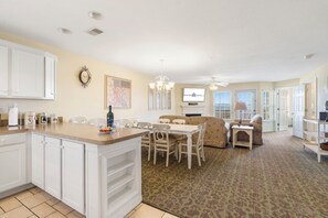 A spacious kitchen with white cabinetry, a dining area with a patterned rug, and a living room with a fireplace.