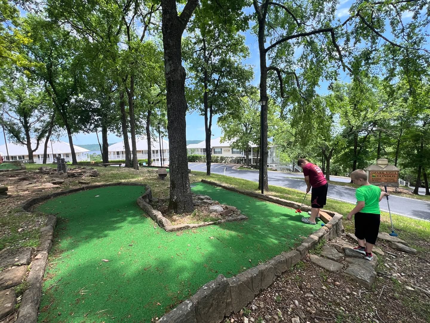 Ein Minigolfplatz mit grünem Spielbereich, umgeben von Bäumen und einer Steinsicht.