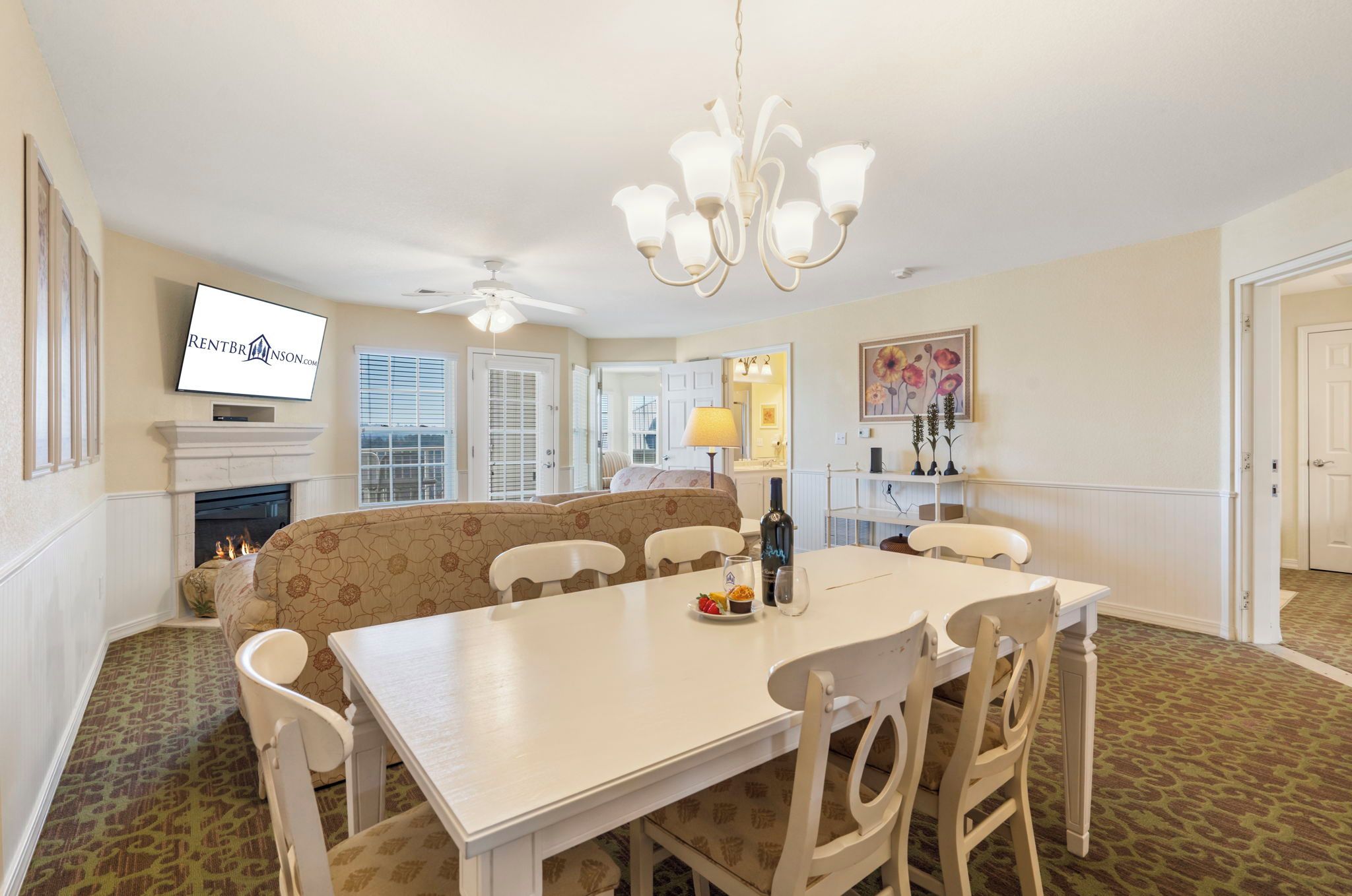 A dining area with a white table and chairs, a sofa, a fireplace, and a television mounted on the wall.