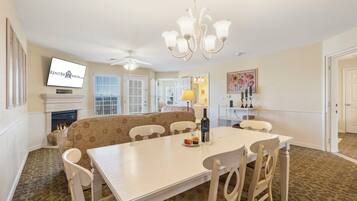 A dining area with a white table and chairs, a sofa, a fireplace, and a television mounted on the wall.