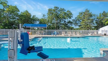 A swimming pool with a lifeguard stand, lounge chairs, and a fenced area with trees in the background.