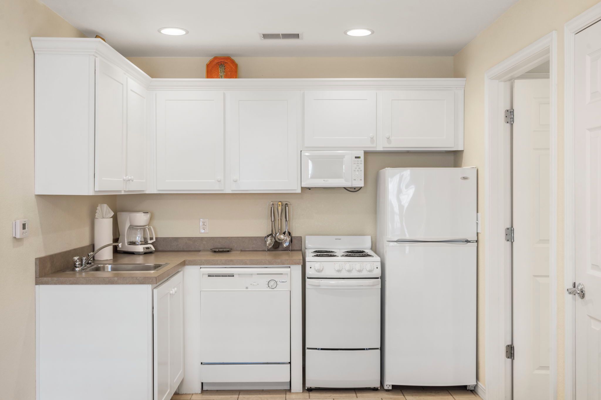 A compact kitchen with white cabinets, a microwave, a stove, and a refrigerator.