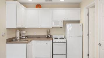 A compact kitchen with white cabinets, a microwave, a stove, and a refrigerator.