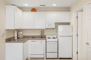 A compact kitchen with white cabinets, a microwave, a stove, and a refrigerator.