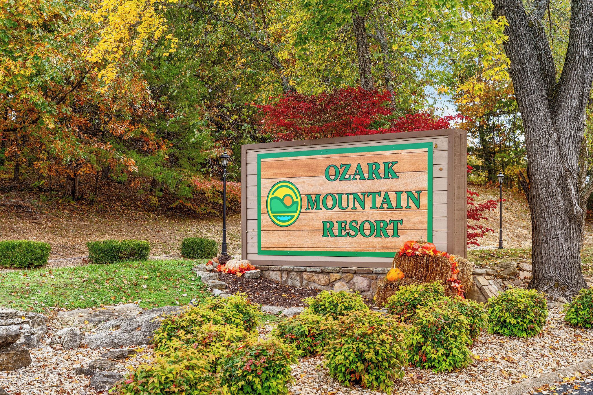 Ein Holzschild für das Ozark Mountain Resort mit einem Logo, umgeben von Herbstlaub und angelegter Bepflanzung.