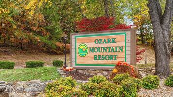 A wooden sign for Ozark Mountain Resort with a logo, surrounded by autumn foliage and landscaping.