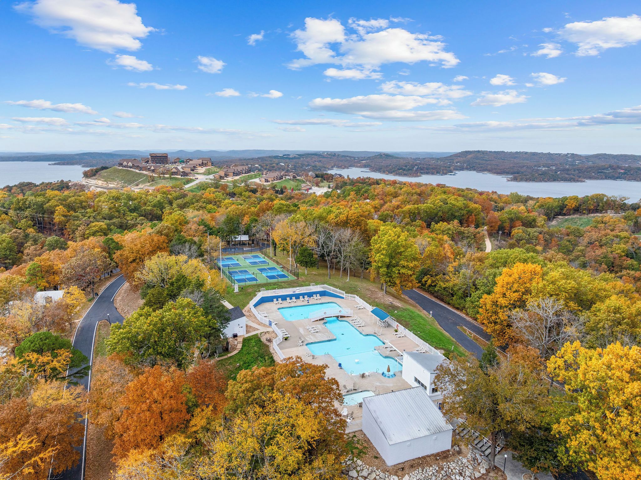 A resort with multiple swimming pools, surrounded by autumn foliage and a lake view.