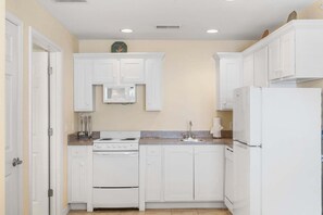 Une cuisine avec des meubles blancs, une cuisinière, un four à micro-ondes et un réfrigérateur.
