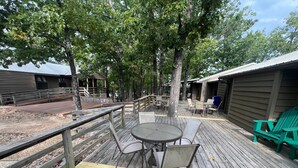 Eine Holzterrasse mit Gartenmöbeln, darunter Tische und Stühle, umgeben von Bäumen.