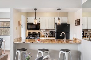 A modern kitchen with white cabinets, a black refrigerator, a granite countertop, and three bar stools. - Near Silver Dollar City, Lake View Condo with Complimentary Daily Tickets (Branson)