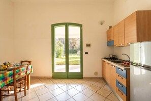 A kitchen with a dining table, chairs, a refrigerator, and a green door leading outside.