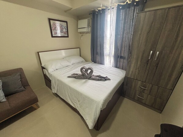 Un dormitorio con cama, un sofá marrón, un armario y un cuadro en la pared.