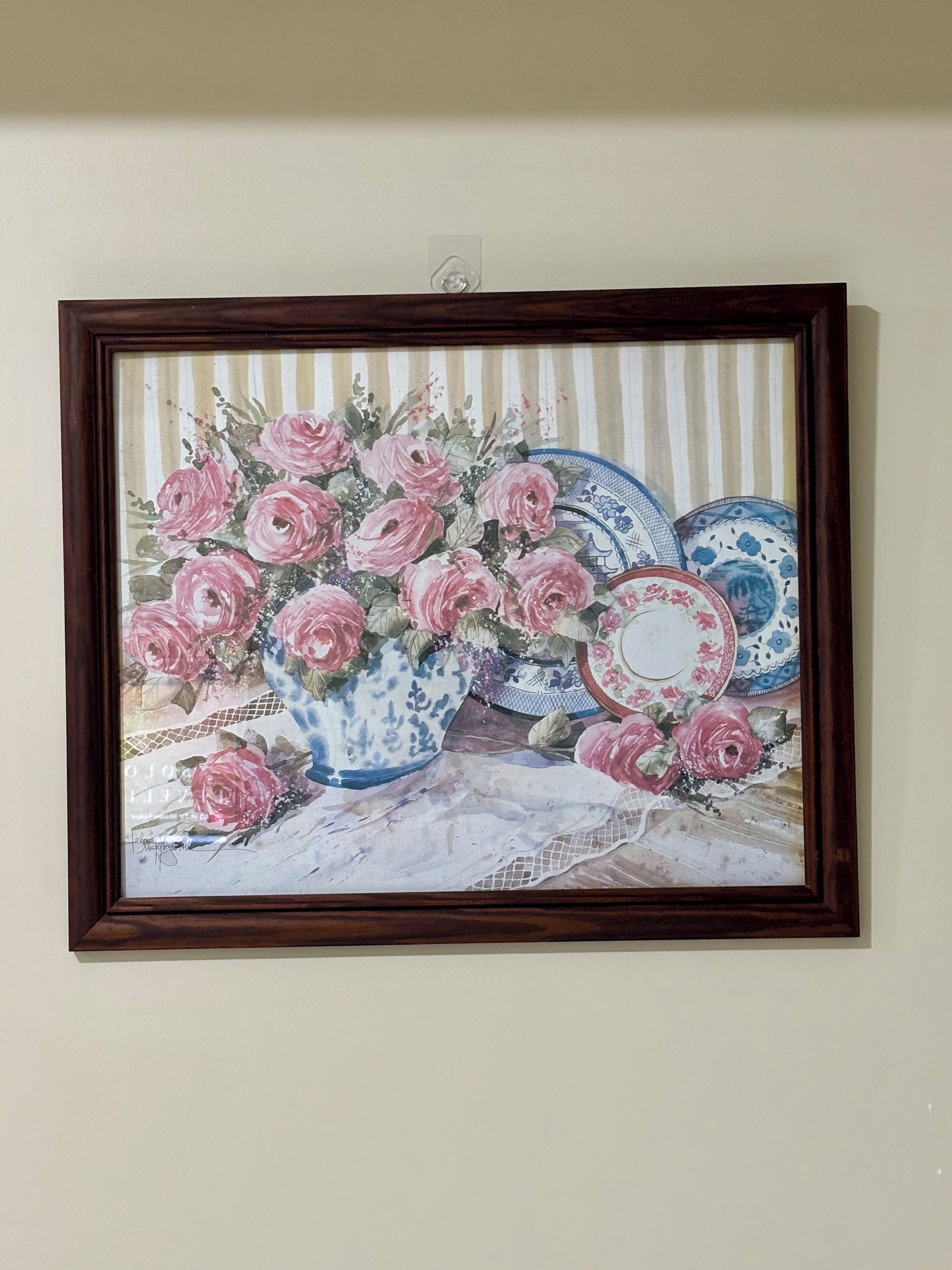 A framed artwork of pink roses in blue and white vases on a table.