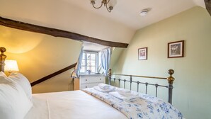 Un lit bien fait, recouvert d’une couvre-lit à motifs floraux, une lampe de chevet et une table de chevet avec une lampe.
