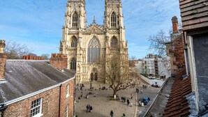 Une cathédrale historique, dotée de deux tours jumelles et d’une grande rosace centrale, qui s’élève au milieu d’une place publique animée par la présence de passants et d’arbres.