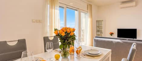 A dining area with a table set for two, a vase with flowers, and a television in the background.