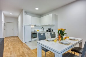 Une cuisine moderne avec des meubles blancs, un four encastré et un coin repas avec une table blanche mise pour deux personnes.