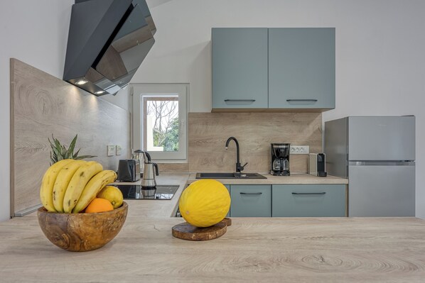 Une cuisine moderne avec des meubles de couleur bleu clair, un plan de travail en bois et un panier de fruits contenant des bananes et une orange.