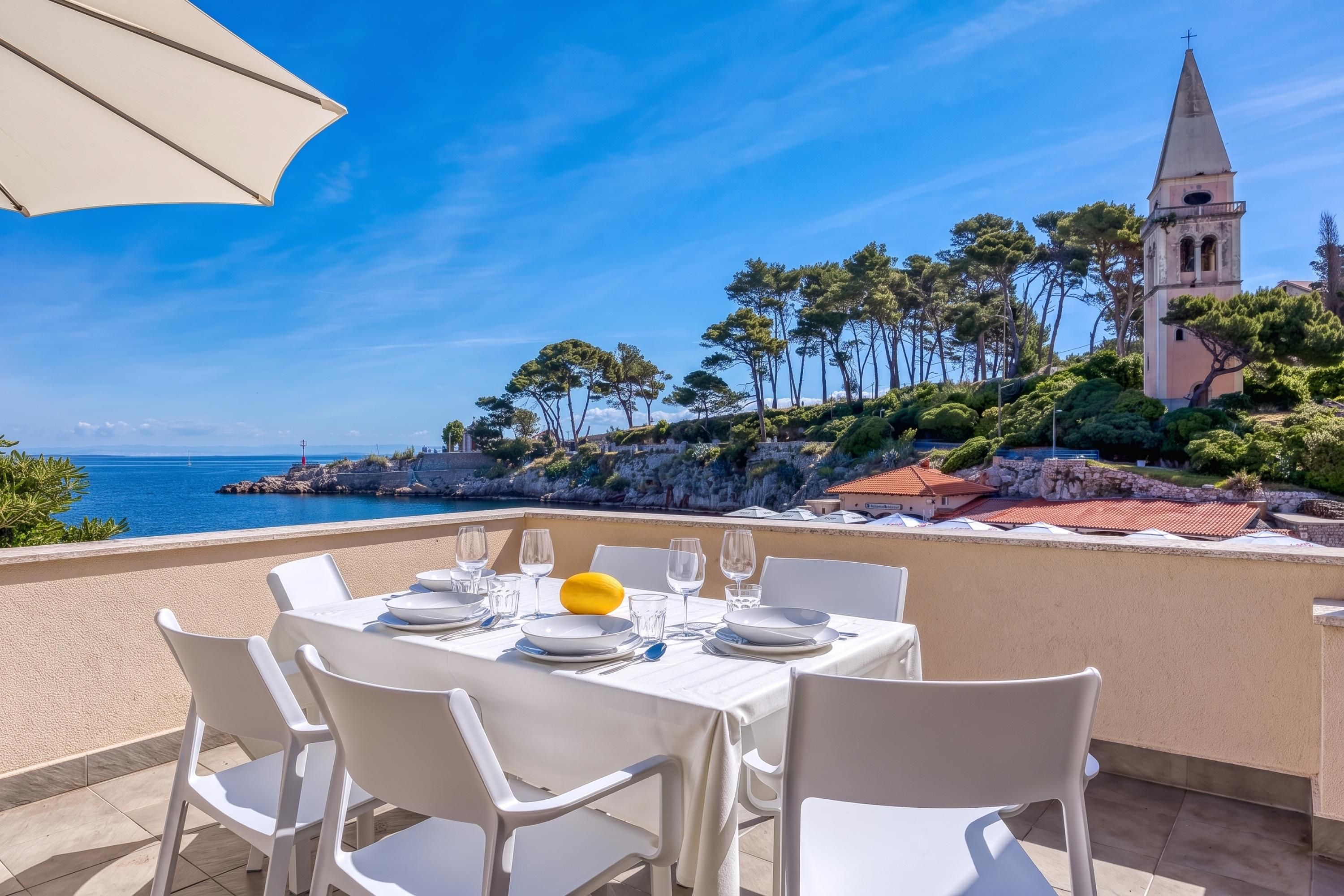 A table set for dining with a view of the sea and a church in the background.