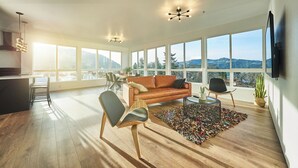A spacious living room with a large window, a sofa, a coffee table, and a dining area. - One-bedroom honeymoon penthouse, Mt Hood views, downtown White Salmon, suite 16 (White Salmon)