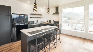 A modern kitchen with a central island, bar stools, and a large window offering a view of the surrounding area. - One-bedroom honeymoon penthouse, Mt Hood views, downtown White Salmon, suite 16 (White Salmon)