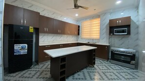 A kitchen with dark brown cabinets, a white countertop, a black refrigerator, a microwave, and an oven. - DJ Villa Your Premium Stay-NS24 (Tema Community 25, Accra-Dawhenya)