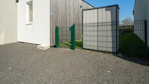 Un edificio con fachada blanca y sección de madera, una puerta verde y un área cercada con camino de grava.