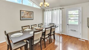 A dining room with a wooden table set for six, six chairs, a chandelier, a framed picture on the wall, and a door with a window view. - 4BR Family Getaway w/ King Bed + 5 TVs, Mins to DC/OldTown,Gameroom,Pet Friendly (Alexandria)