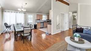 A spacious living area with hardwood flooring, a dining table set for four, a kitchen with wooden cabinets, and a ceiling fan. - 4BR Family Getaway w/ King Bed + 5 TVs, Mins to DC/OldTown,Gameroom,Pet Friendly (Alexandria)