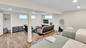 A modern, well-lit room with a sofa, a TV, a desk, and two beds. - 4BR Family Getaway w/ King Bed + 5 TVs, Mins to DC/OldTown,Gameroom,Pet Friendly (Alexandria)