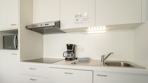 Een moderne keuken met witte kasten, een ingebouwde magnetron, een koffiezetapparaat en een roestvrijstalen spoelbak.