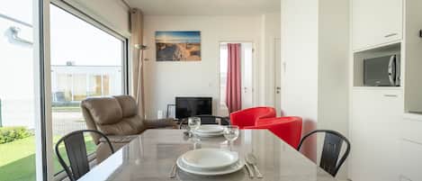 A modern dining area with a glass table, black and red chairs, a television, and a painting on the wall.