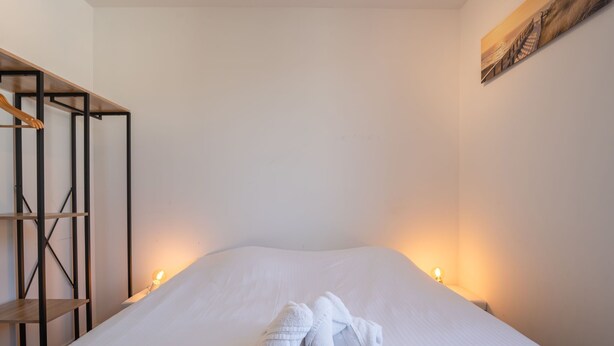 Een netjes opgemaakt bed met twee handdoeken gevouwen aan het voeteneinde, een houten plankenwand aan de linkerzijde en een schilderij aan de muur.