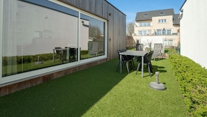 Een modern gebouw met grote glasramen, een houten gevel en een verzorgd gazon met een tafel en stoelen.