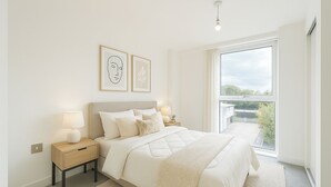 A bedroom with a large bed, bedside tables with lamps, a view of the outdoors through a large window, and two framed artworks on the wall. - Not available (Salford)