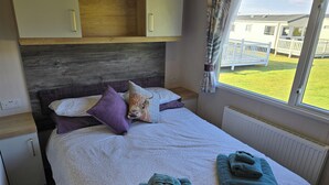 A bedroom with a bed, pillows, a headboard, a window with a view, and a radiator. - 3 Bed-Sleeps 8-Free Parking-5 Min to Beach (Dornoch)