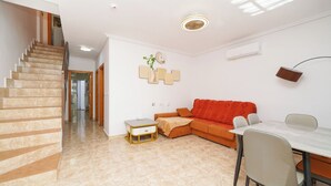 Una sala de estar moderna con una escalera, un sofá rojo, una mesa de comedor con sillas y una pequeña mesita auxiliar.