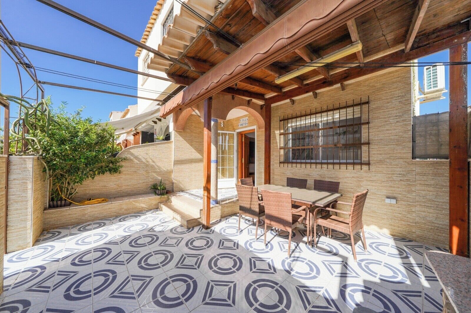 A covered patio with a tiled floor, a table with chairs, and a wooden pergola.