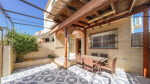 Un porche cubierto con suelo de baldosas, una mesa con sillas y una pérgola de madera.