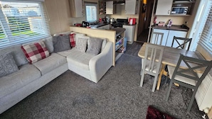 En kompakt opholdsstue med sofa, spisebord og tekøkken.