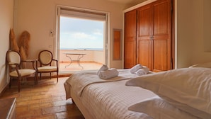 A hotel room with a bed, a chair, a table, and a view of the beach. - Magnificent Provençal Villa with Swimming Pool and Sea View (Antibes)
