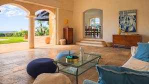 A spacious living area with a glass coffee table, comfortable seating, and a view of a lush garden and pool. - Magnificent Provençal Villa with Swimming Pool and Sea View (Antibes)