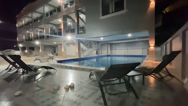 Un edificio de varios pisos con piscina y sillones de descanso.