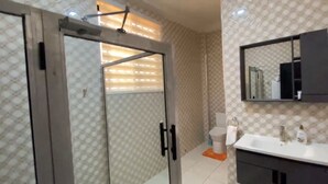 Un baño con puerta de vidrio, un lavamanos blanco, un espejo y papel tapiz estampado.