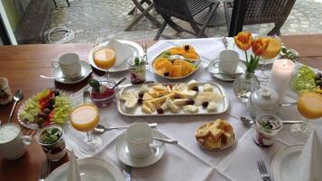 Una mesa de desayuno servida con platos, vasos y una variedad de alimentos, entre ellos frutas, quesos y pan.