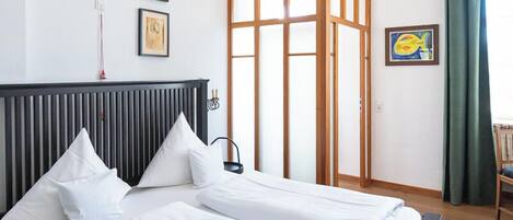 Une chambre avec un grand lit, un plancher en bois, un lustre et une porte coulissante donnant sur un balcon.
