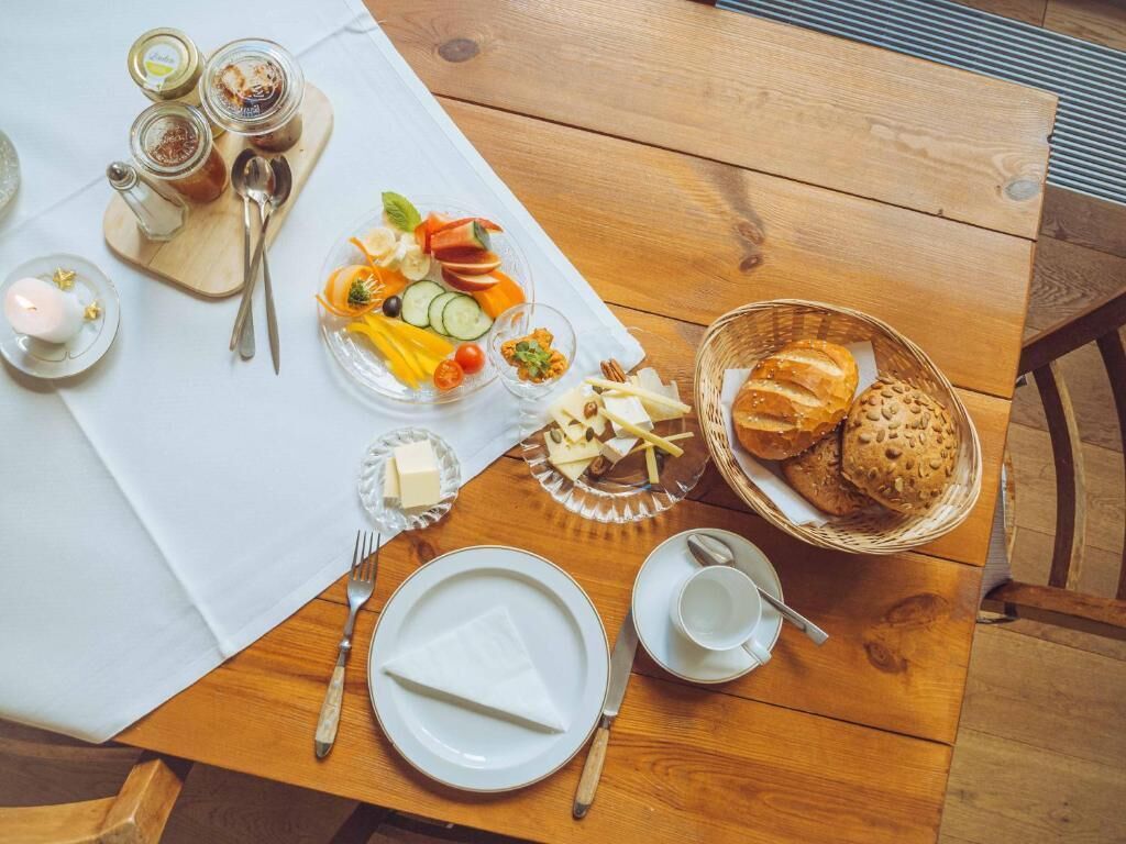 Una mesa de madera dispuesta con diversos alimentos, incluyendo una bandeja de frutas, queso, pan y salsas.