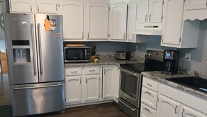A modern kitchen with white cabinets, stainless steel appliances, a microwave, toaster, coffee maker, and a built-in oven.