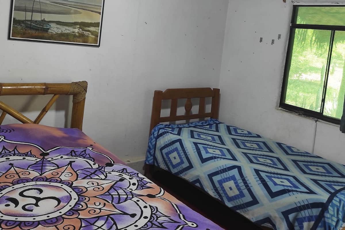 Um quarto pequeno com uma cama, uma cadeira, uma janela e um quadro na parede.