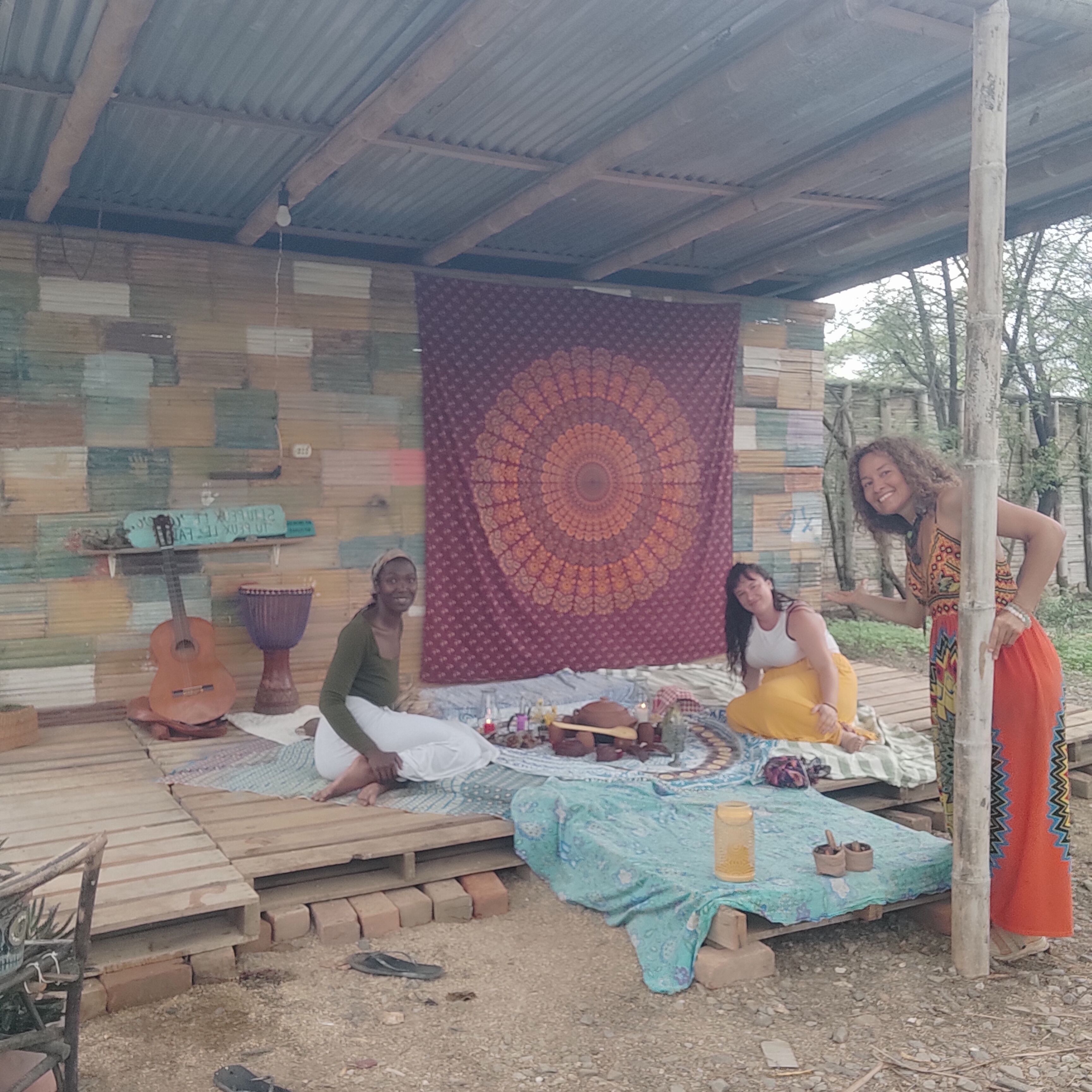 Un cadre extérieur rustique avec une terrasse en bois, une grande tapisserie et une guitare.